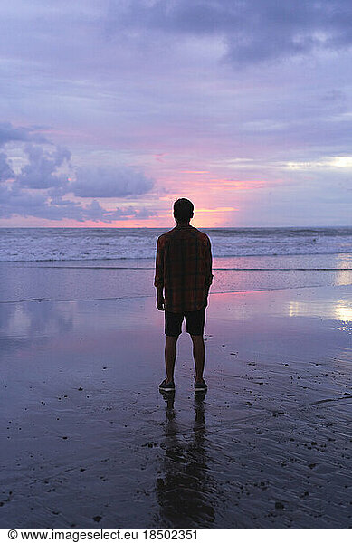 A man on the ocean watching the sunset on the beach.