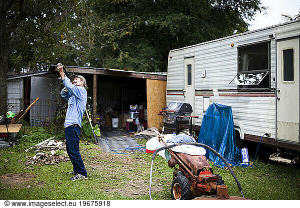 A man points a pellet gun at a squirrel in his backyard filled with trash and a trailer home.
