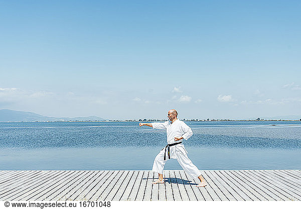 A man practices martial arts on a wooden walkway near the water