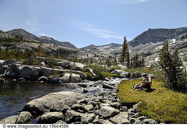 A man relaxes and cleans up at a pristine pool of water on the Sierra High Route in Kings Canyon National Park  CA.