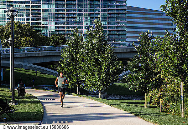 A man runs on a pathway in a city park in early morning light