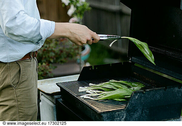 A man's hand putting seasoned wild ramps on the grill