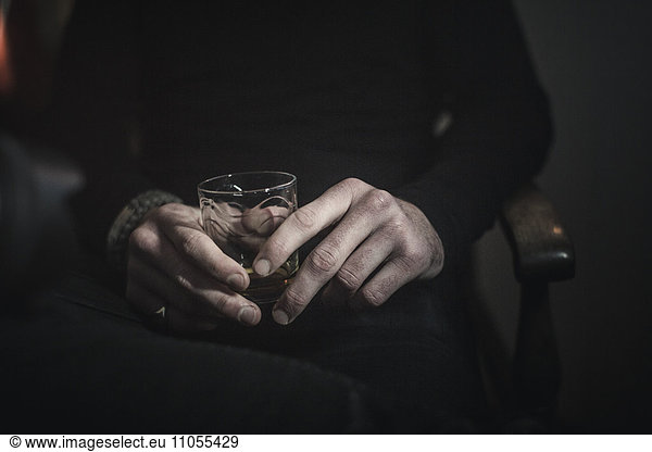 A man's hands holding a glass of whisky.