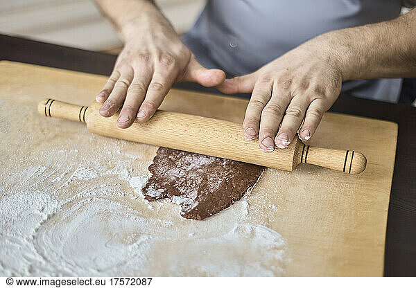 A man's hands roll out the chocolate dough with a rolling pin