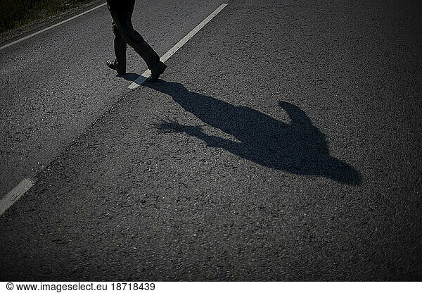A man's shadow is cast as he crosses a road after picking wild asparagus near Villamartin village  Cadiz province  Andalusia  Spain.