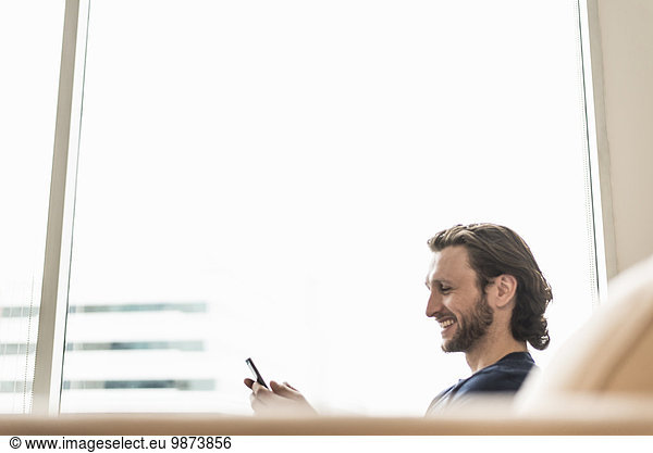A man seated checking his smart phone and laughing.