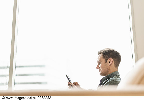 A man seated holding a smart phone checking his messages.