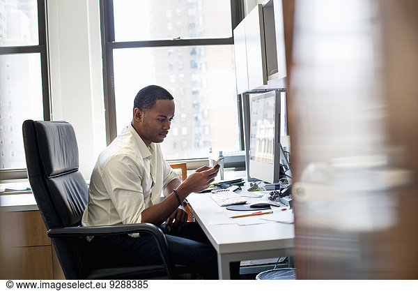A man sitting in an office  checking his smart phone.