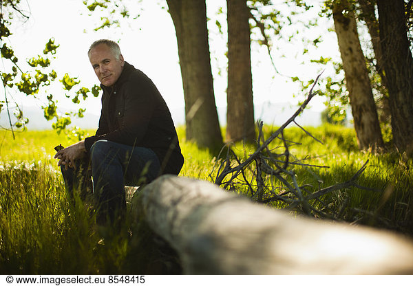 A man sitting on a fallen tree trunk in woodland.