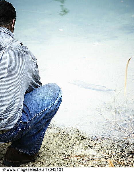 A man squatting down at the waters edge.