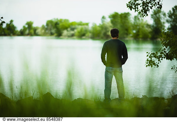 A man standing alone looking into the distance across the water  deep in thought.