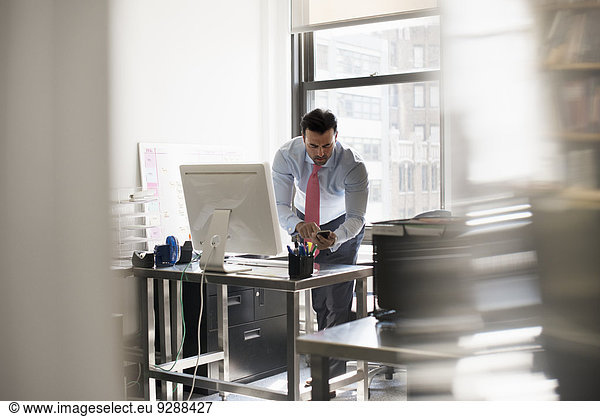 A man standing at his desk using his phone  dialling or texting.