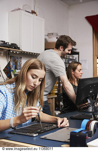 A man standing behind two women sitting working on circuitry in a technology lab.