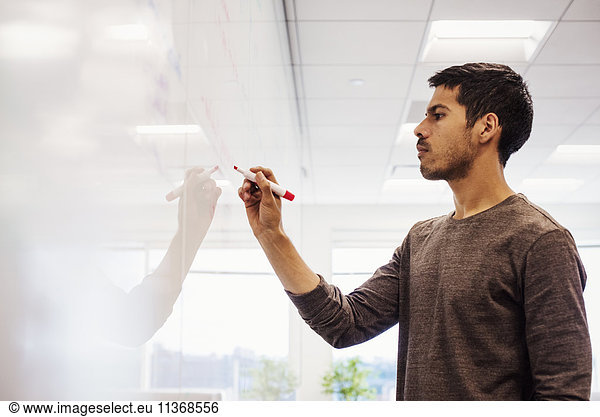 A man standing in a classroom writing on a whiteboard.