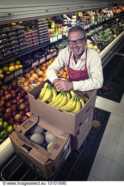 A man standing in a grocery shop beside a display of fresh fruits and vegetables.