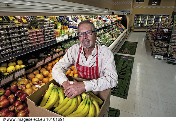 A man standing in a grocery shop beside a display of fresh fruits and vegetables.