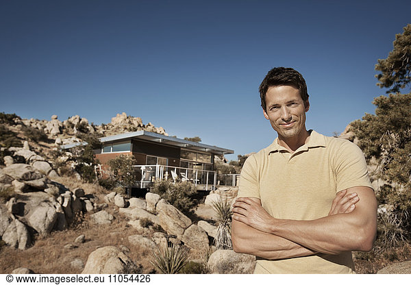 A man standing in front of an eco home  designed to blend into the rocky hilllside of a desert landscape. Sustainable architecture with a low impact.