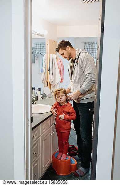 A man standing in the bathroom brushing his child's hair.