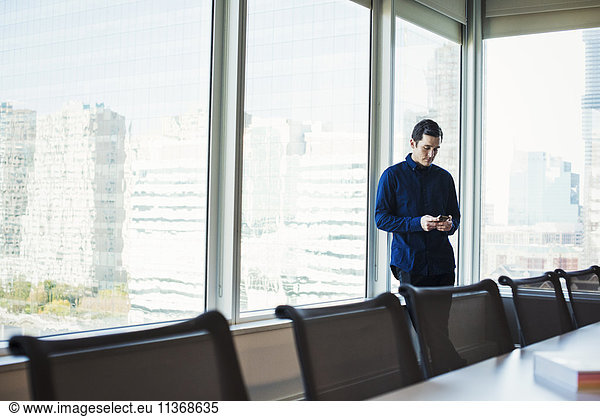 A man standing next to a table in a meeting room looking at a cellphone.