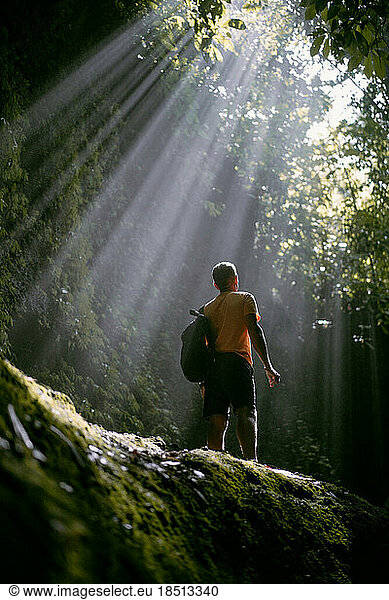 A man standing on a stone in the light looks up.