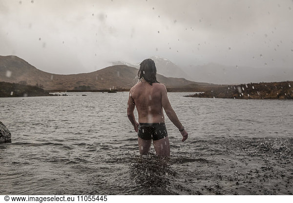 A man standing thigh deep in sea water in swimming trunks.