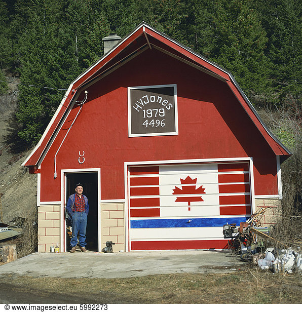 A man stands in the doorway beneath two lucky horseshoes  beside a door painted with the Canadian flag  at a patriotic workshop near Vernon  British Columbia  Canada  North America