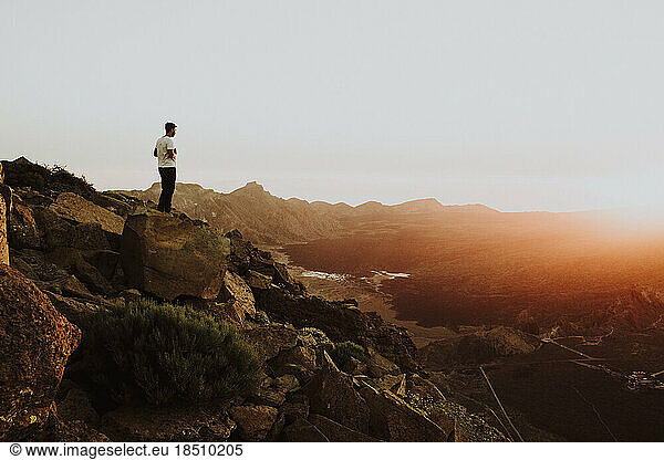A man stands on mountain top watching sunset