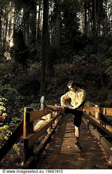 A man stops to stretch on a wooden bridge while trail running through the Olympic National Park.