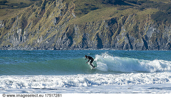 A man surfs the cold waters of Kodiak Alaska in a wet suit in the fall