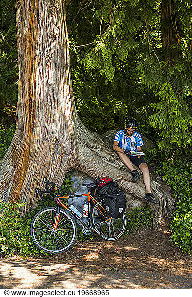 A man takes a break while sitting on a log near his bicycle on the famous and scenic Chuckanut Drive near Bellingham  WA.