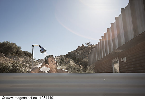A man taking a shower outdoors on the terrace of a low impact eco house.