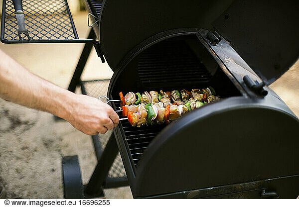 A man turning the colorful chicken skewers on the grill.
