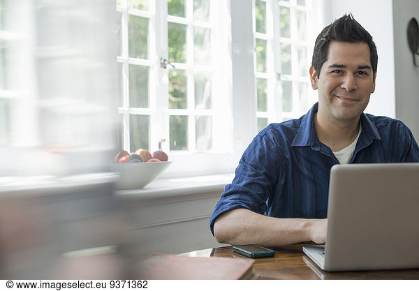 A man using a laptop seated at a table by a window. Working from home.