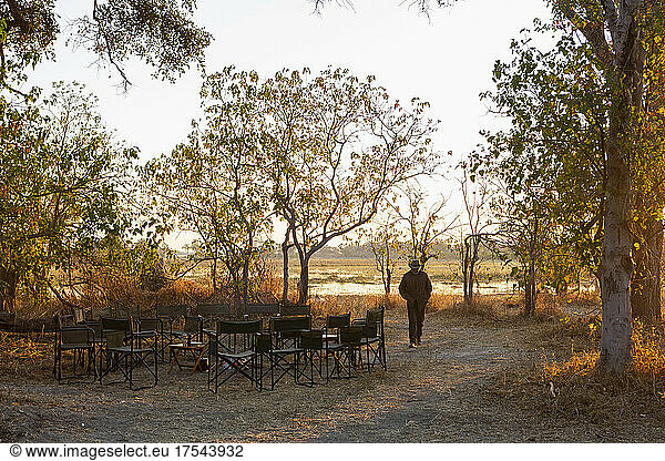 A man walking on a path at a safari camp by a water pool