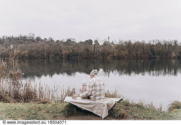 A man with a baby girl are resting near the river and drinking tea