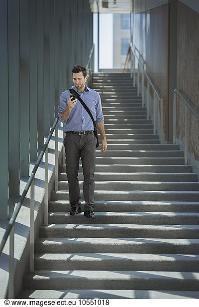 A man with a laptop bag walking down steps  using a smart phone.