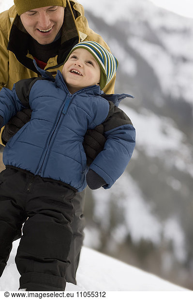 A man with a young child wrapped up against the cold  in the mountains in snow.