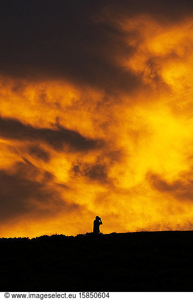A man with binoculars against a brilliant orange clouded sky at sunset