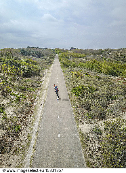 A man with long hair skating on a empty road in europe