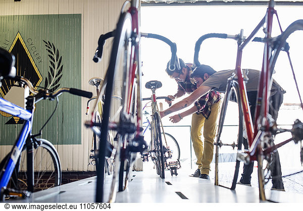 A man working in a bicycle repair shop  checking a bike with a customer.