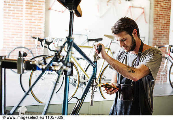A man working in a bicycle repair shop pausing to check his messages.