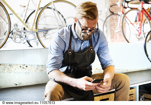 A man working in a bicycle repair shop sitting checking his phone for messages. Coffee break.