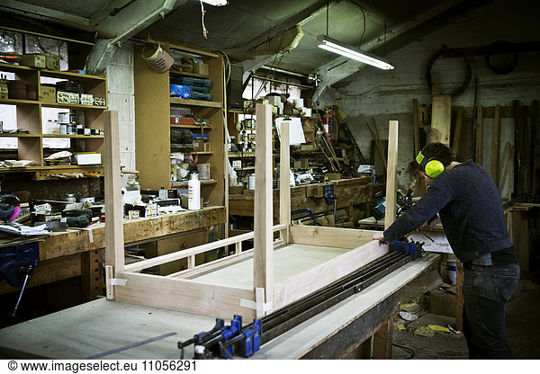 A man working in a furniture maker's workshop  assembling a table.