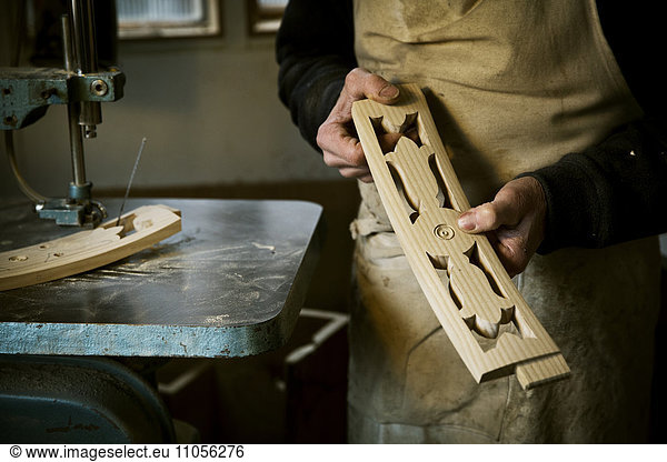 A man working in a furniture maker's workshop holding shaped carved chair back struts.