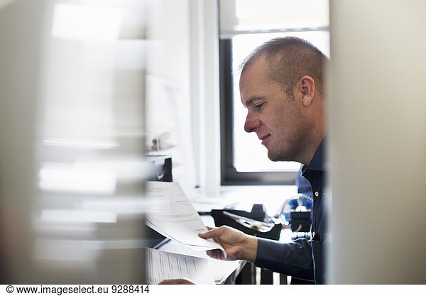 A man working in an office  reading paperwork.