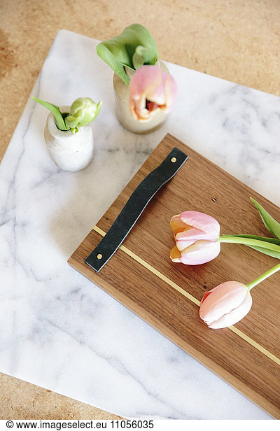 A marble slab with two vases and pink tulips and a wooden board with handle.