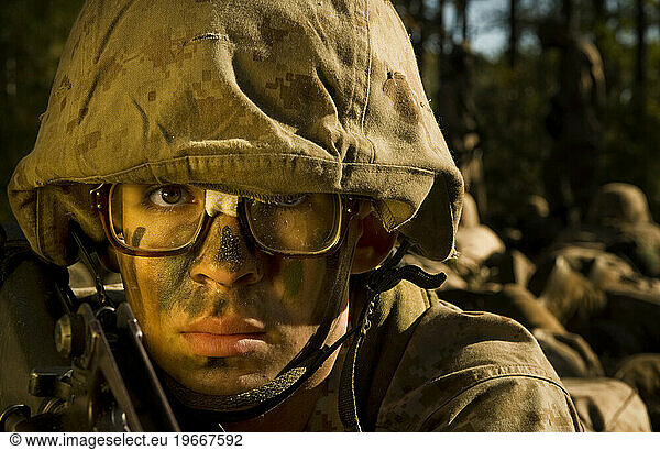 A marine recruit has tape holding together his military issued glasses during a field training exercise. He is wearing a desert camouflage uniform and helmet.