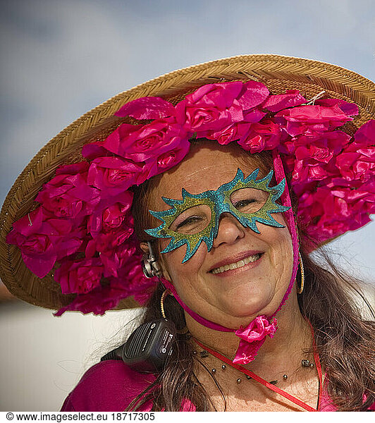 A masked woman with a colorful hat at a parade in Santa Barbara. The parade features extravagant floats and costumes.