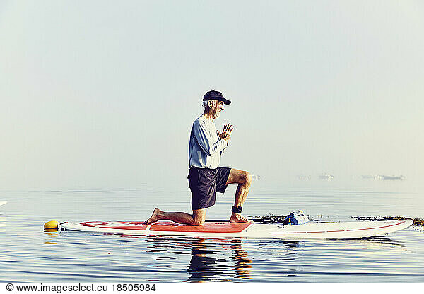 A mature male standup paddle boarder doing yoga at sunrise in the fog