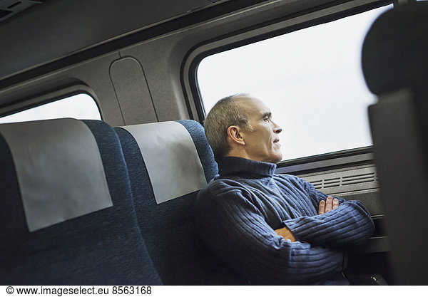 A mature man sitting in a window seat on a train journey  looking out into the distance.